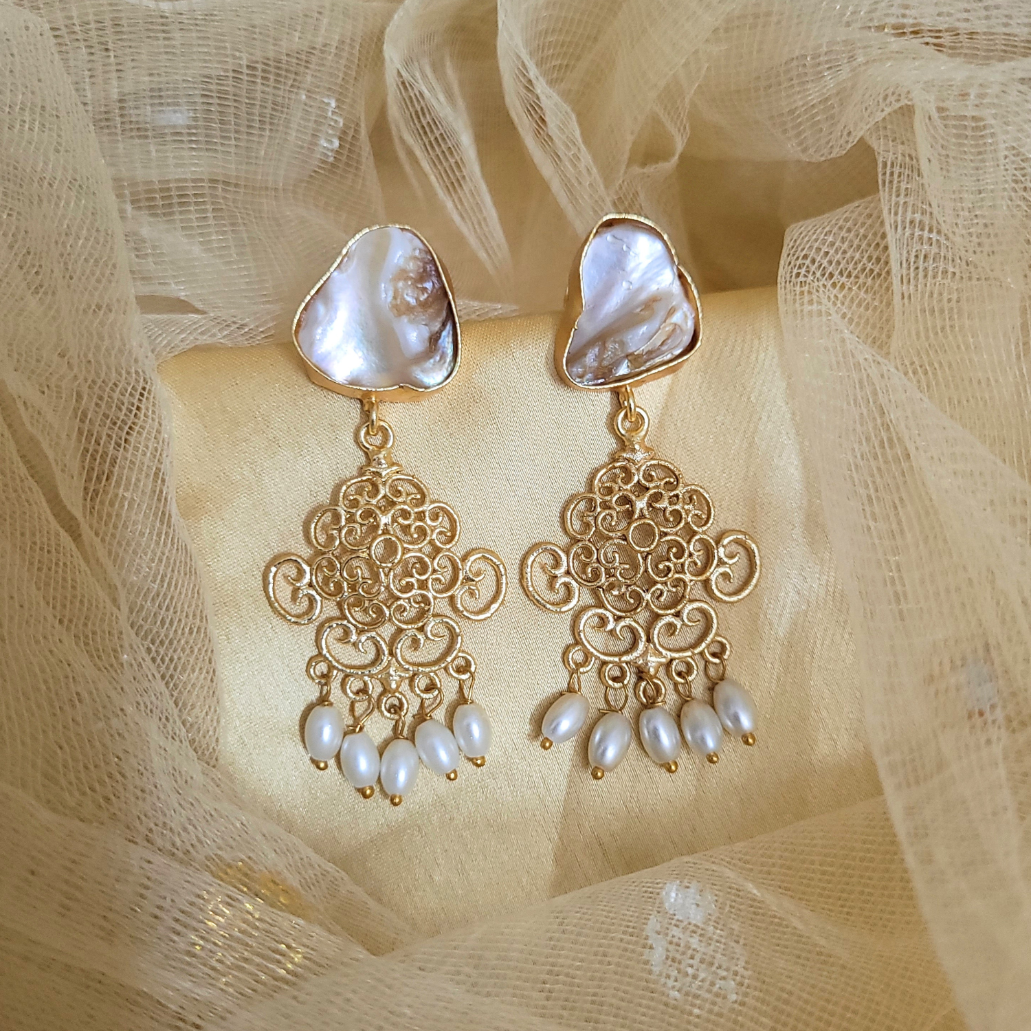 Gold earrings with pearl accents on a beige fabric background