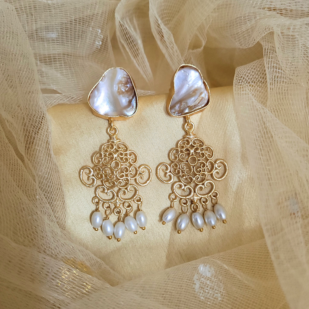 Gold earrings with pearl accents on a beige fabric background