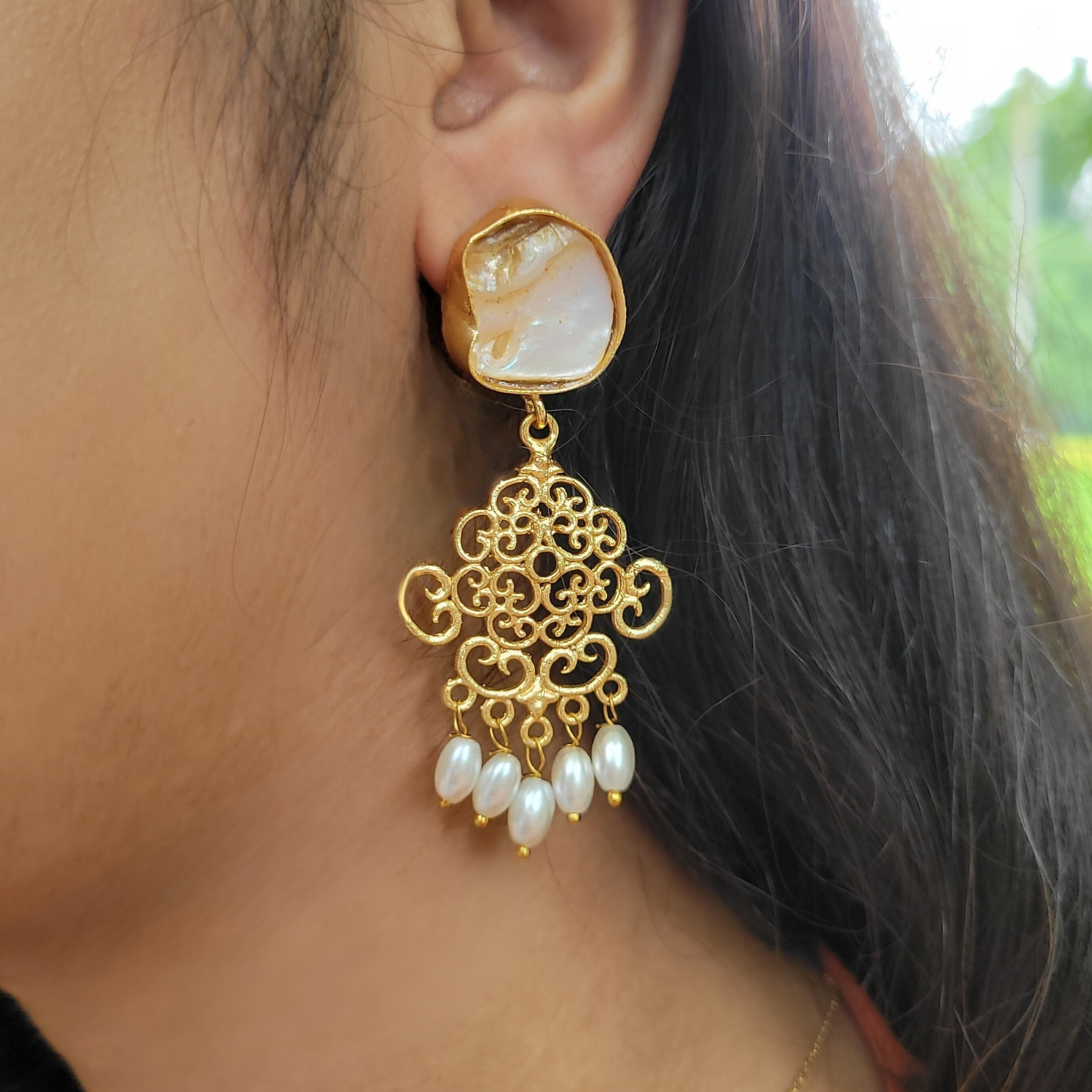 Gold earring with pearl drops worn by a person. Earrings have baroque pearls studs, swirl geometric pattern and rice pearl danglers at the end.