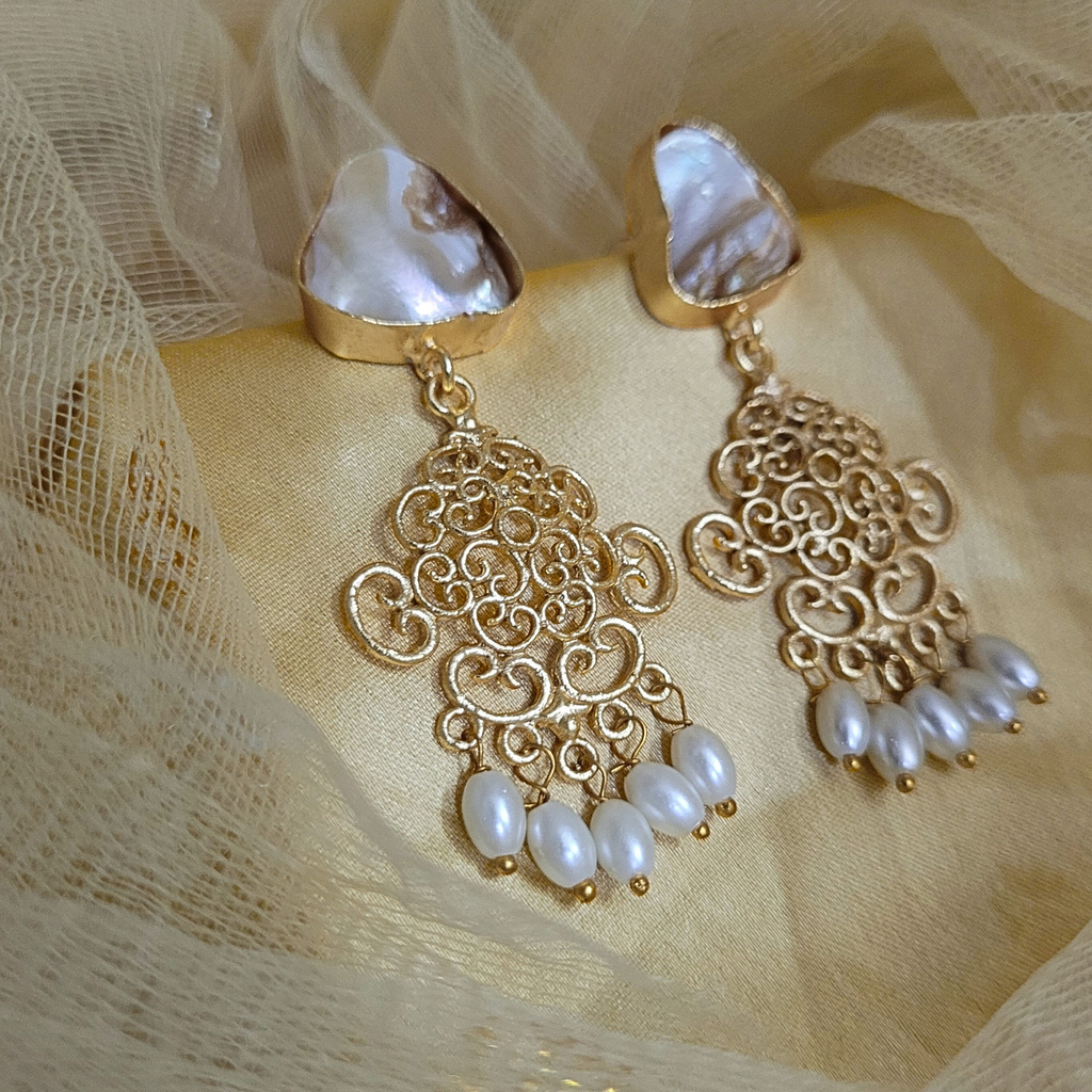 Gold earrings with pearl drops on a beige fabric background