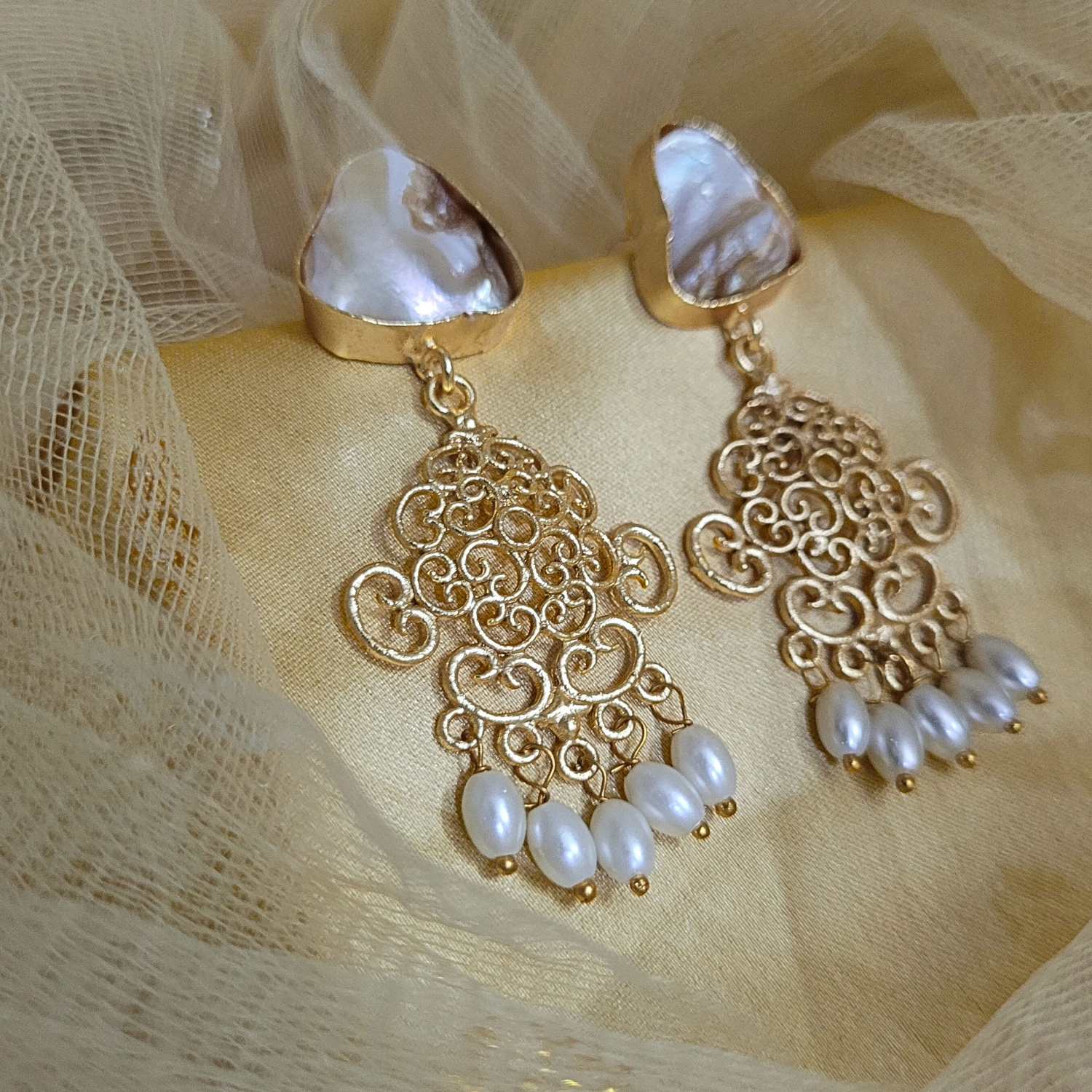 Gold earrings with pearl drops on a beige fabric background