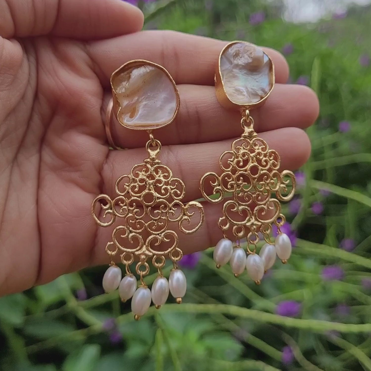 Lovely golden dangling earrings in hand. Moving softly with breeze. Earrings have baroque pearls studs, swirl geometric pattern and rice pearl danglers at the end.