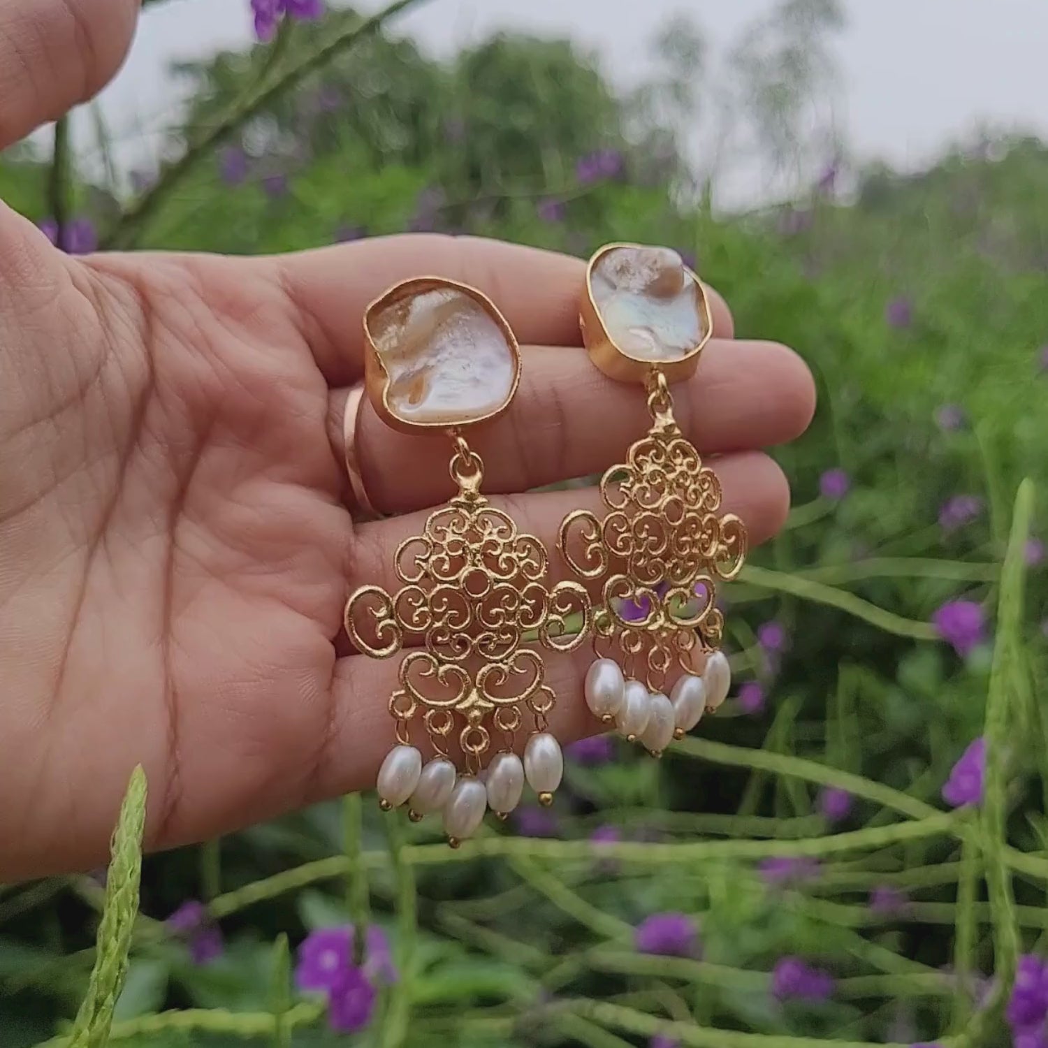 Lovely golden dangling earrings in hand. Moving softly with breeze. Earrings have baroque pearls studs, swirl geometric pattern and rice pearl danglers at the end.